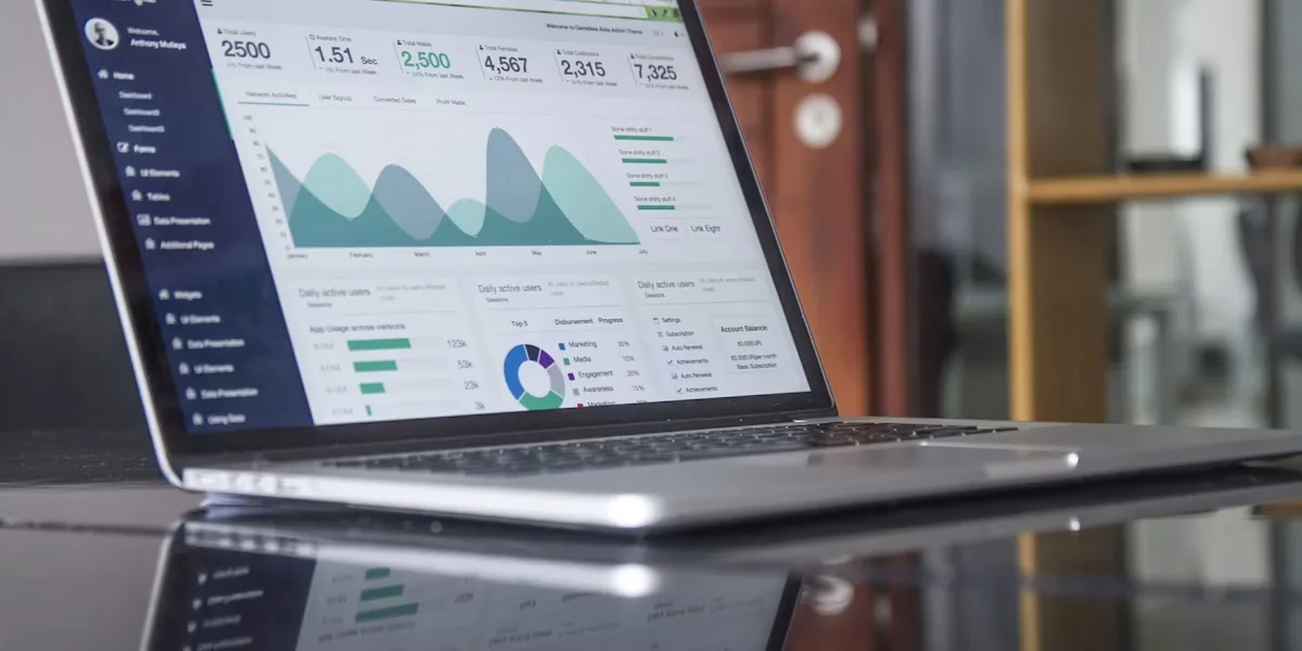 An open laptop displays a colourful analytics dashboard on a reflective table, with a door and windows behind it; no people.