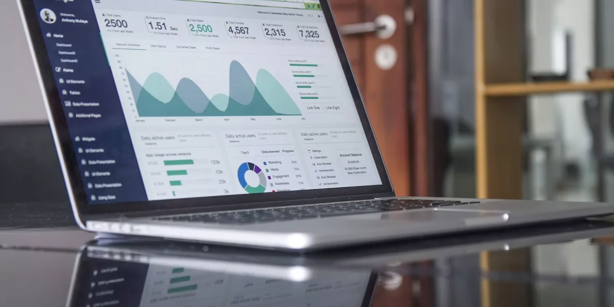Open laptop displaying charts and dashboard data on a reflective table, indoors near a door; no people.