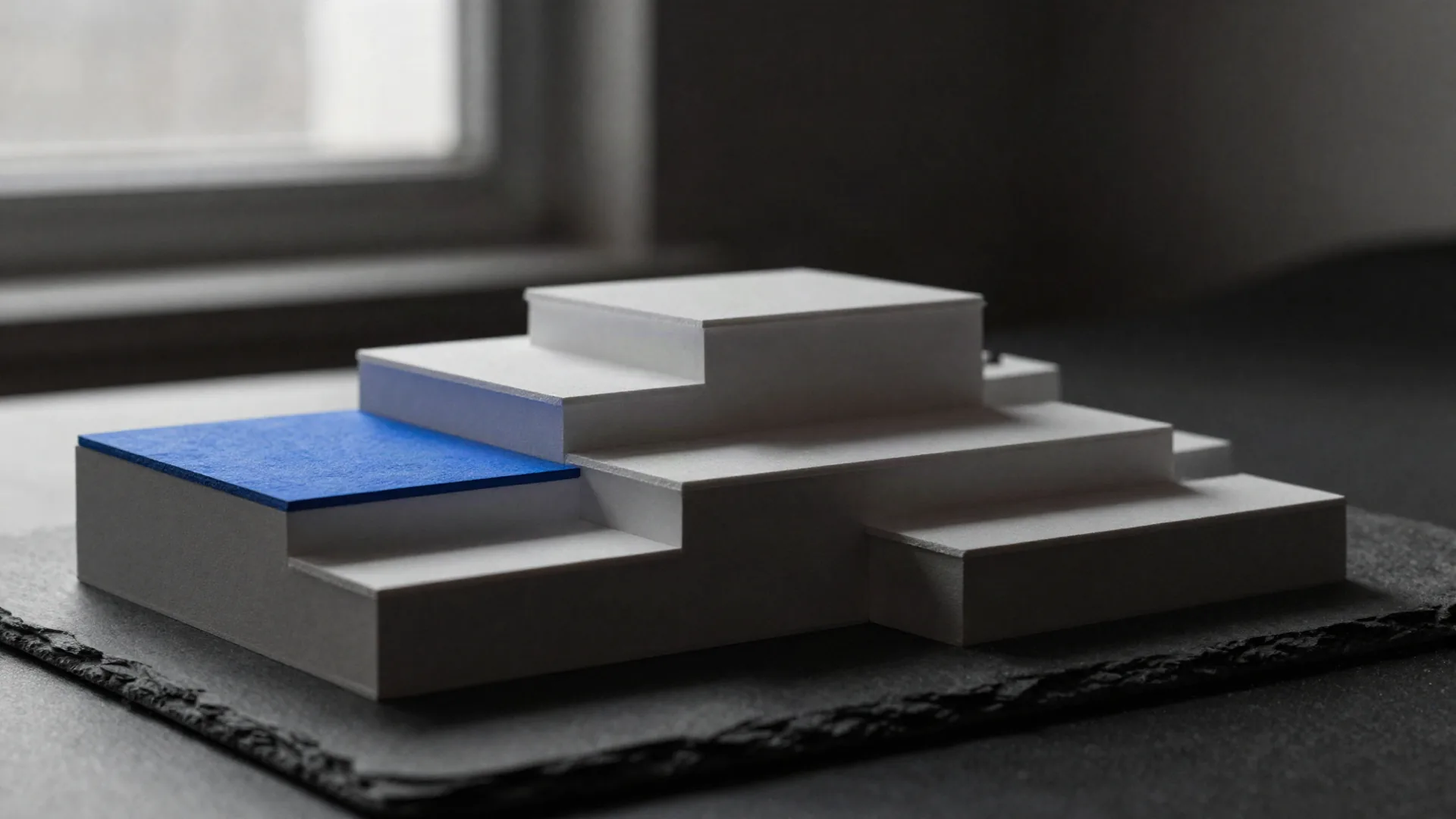 A white architectural model of four terraced steps, the lowest picked out in blue